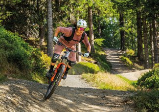 Eine Mountainbikerin fährt auf einem schmalen Trail durch einen dicht bewaldeten Wald.