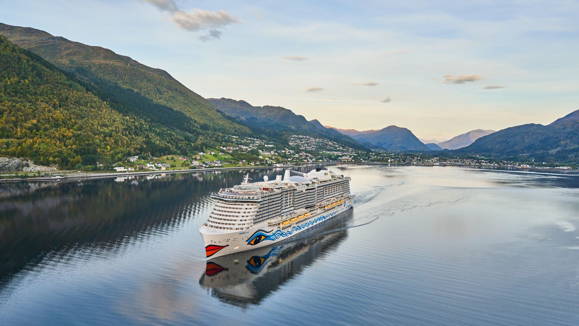 AIDAnova in Norwegen, links Häuser eines Ortes und Berge | © AIDA