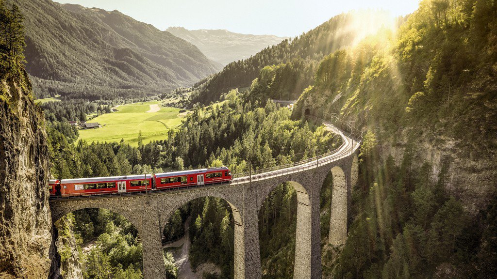 Der Glacier Express überquert bei strahlendem Sonnenschein eine Brücke inmitten einer beeindruckenden Schweizer Berglandschaft | © DERTOUR