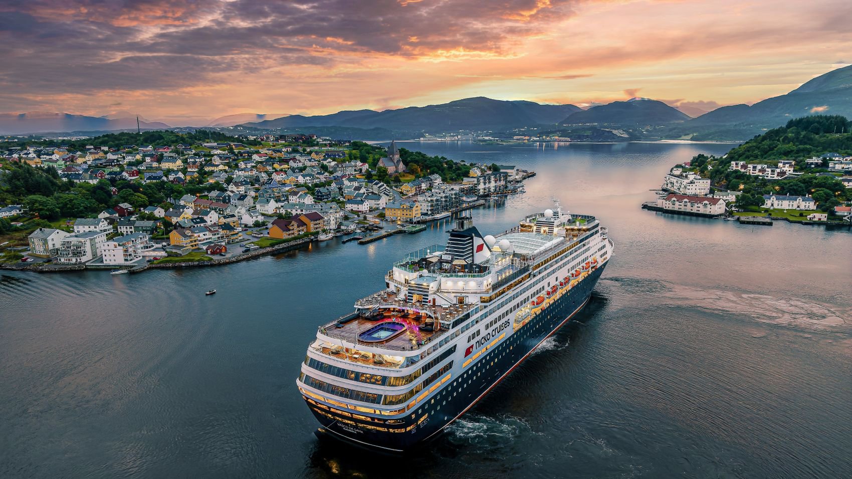 Luftaufnahme von Kristiansund mit der VASCO DA GAMA, umgeben von Küstenstadt, Hafenanlagen und dem Meer unter klarem Himmel | © Nicko Cruises