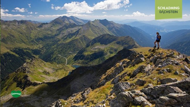 Eine Wanderin steht oben auf einem Berg und blickt in die beeindruckende alpine Landschaft.