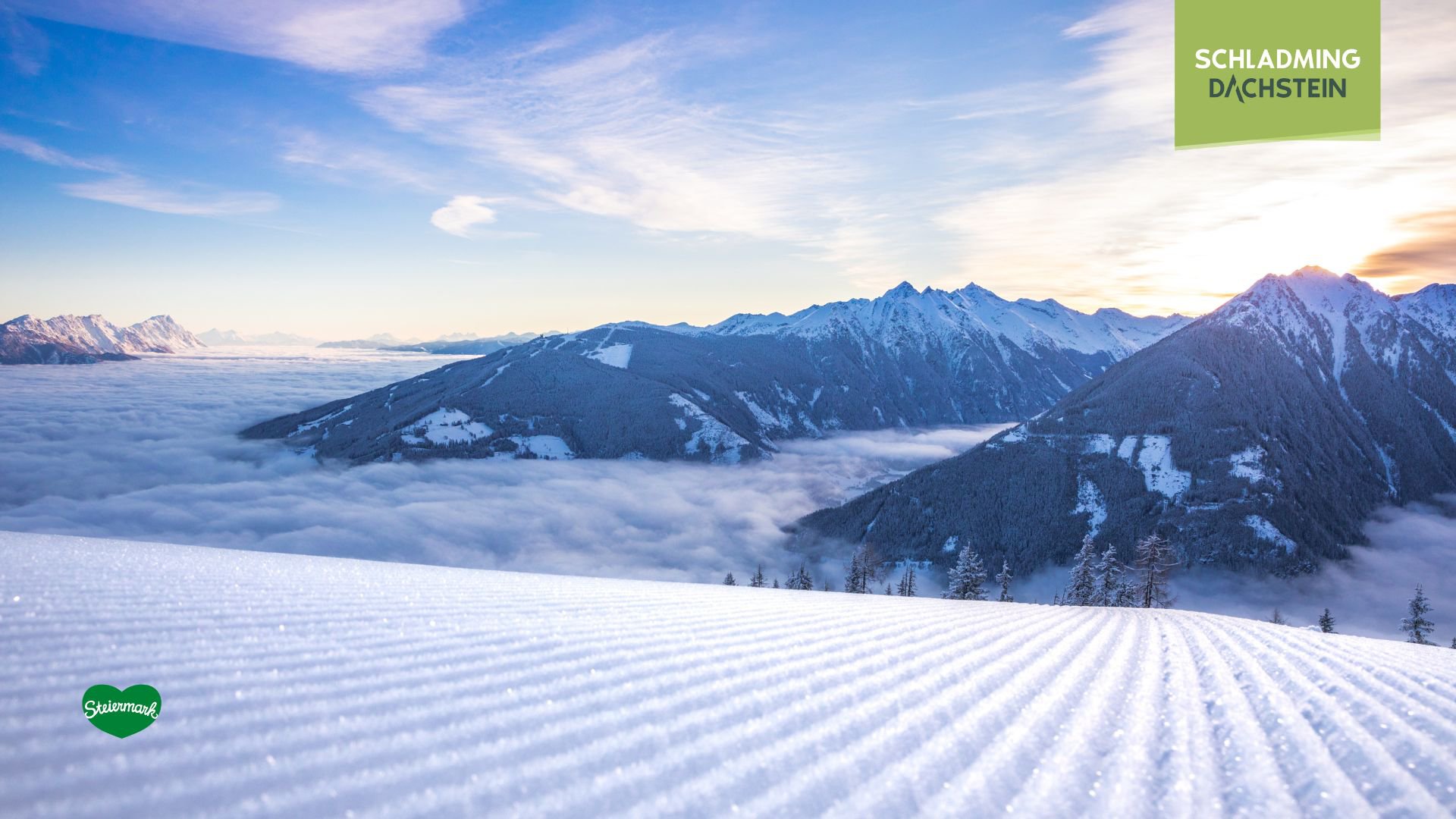 Frisch präparierte Skipiste, verschneite Gipfel und ein atemberaubendes Bergpanorama mit Nebelschicht in den Morgenstunden.