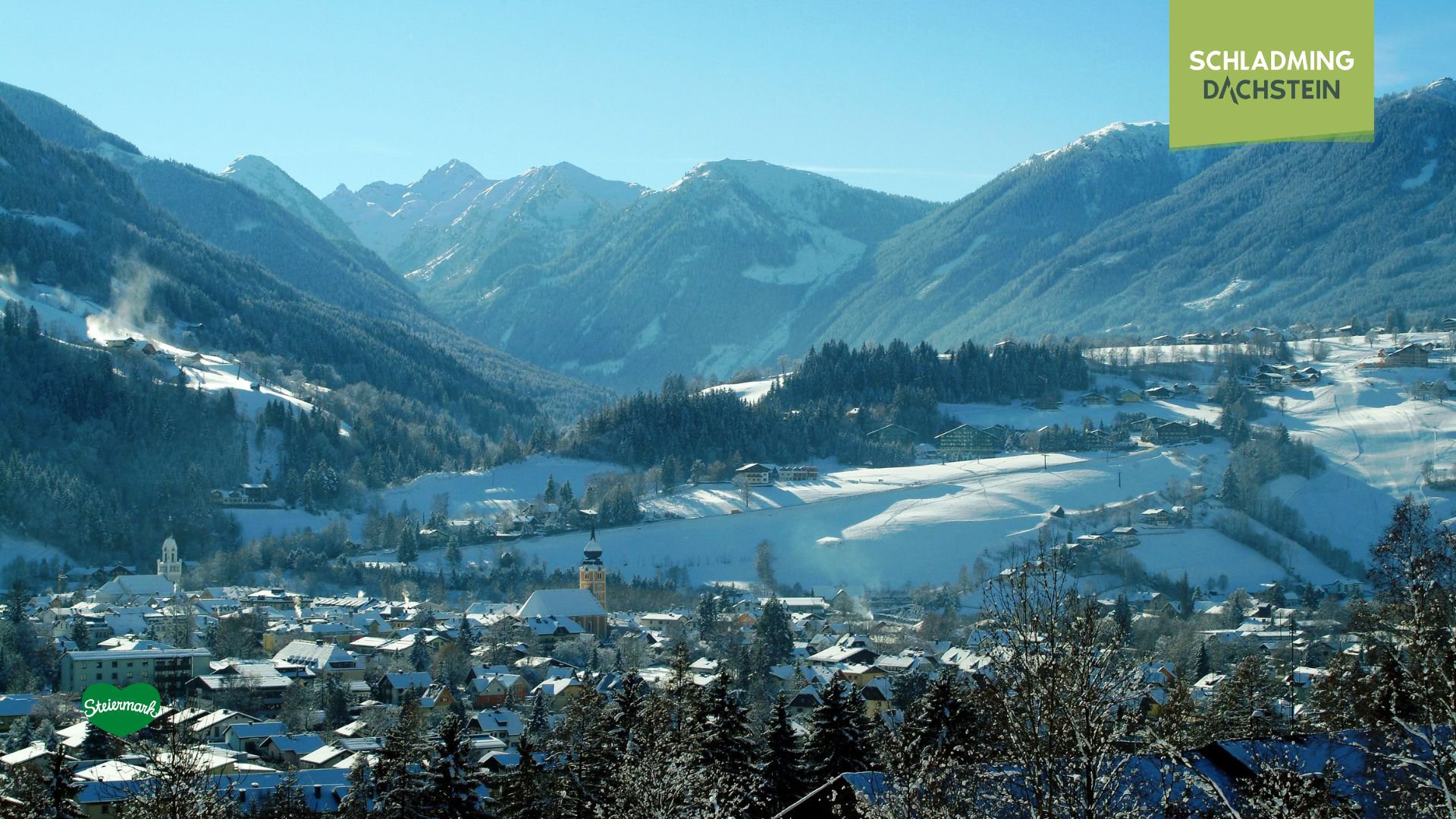 Winterliche Berglandschaft mit einem schneebedeckten Tal und einem kleinen Dorf im Vordergrund.