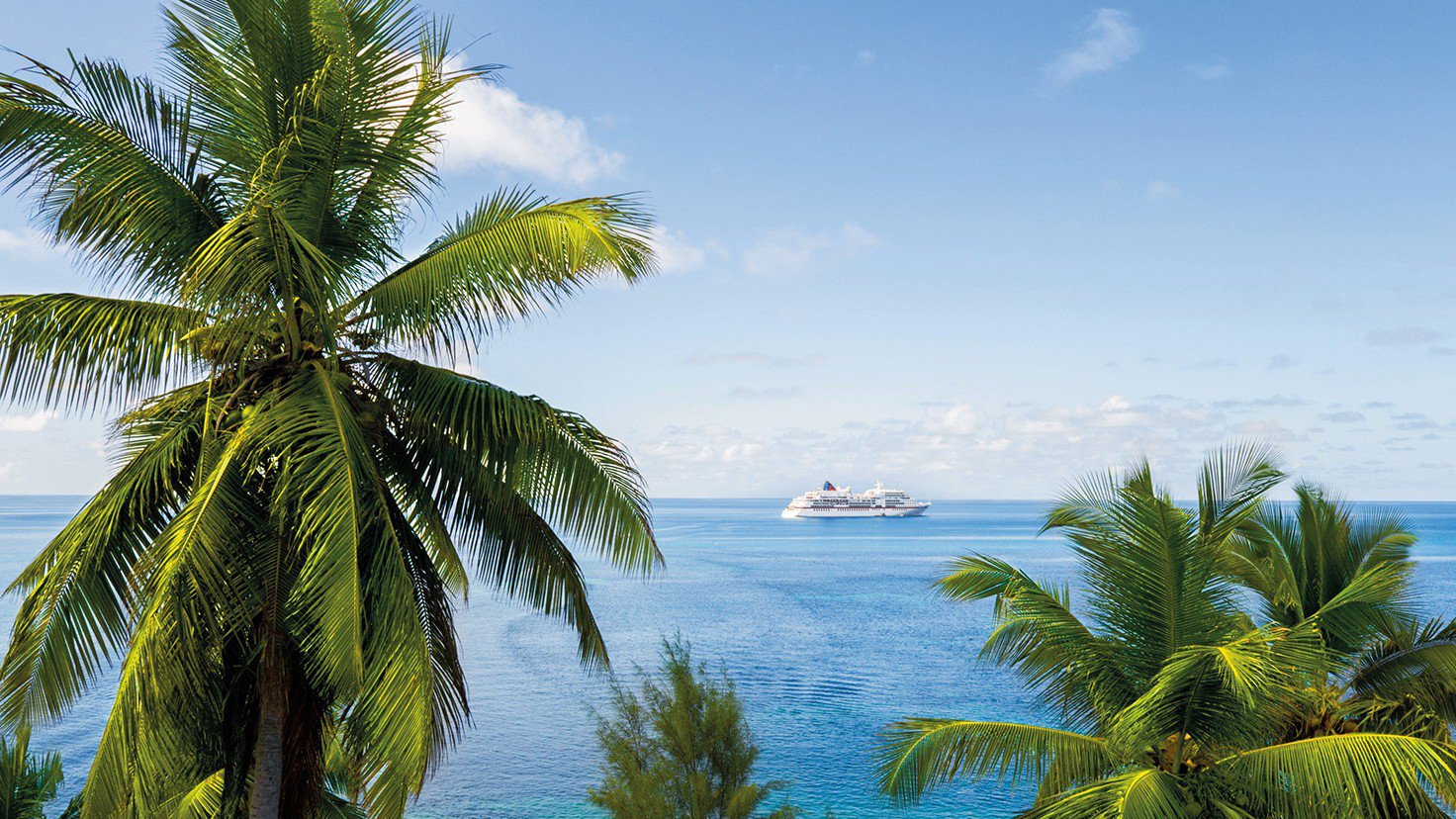 Die EUROPA fährt auf dem Meer, umgeben von Palmen im Vordergrund | © Hapag-Lloyd Cruises