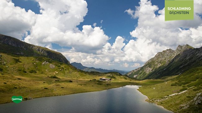 Bergsee mit wunderschönem Bergpanoramablick und einer gemütlichen Hütte.