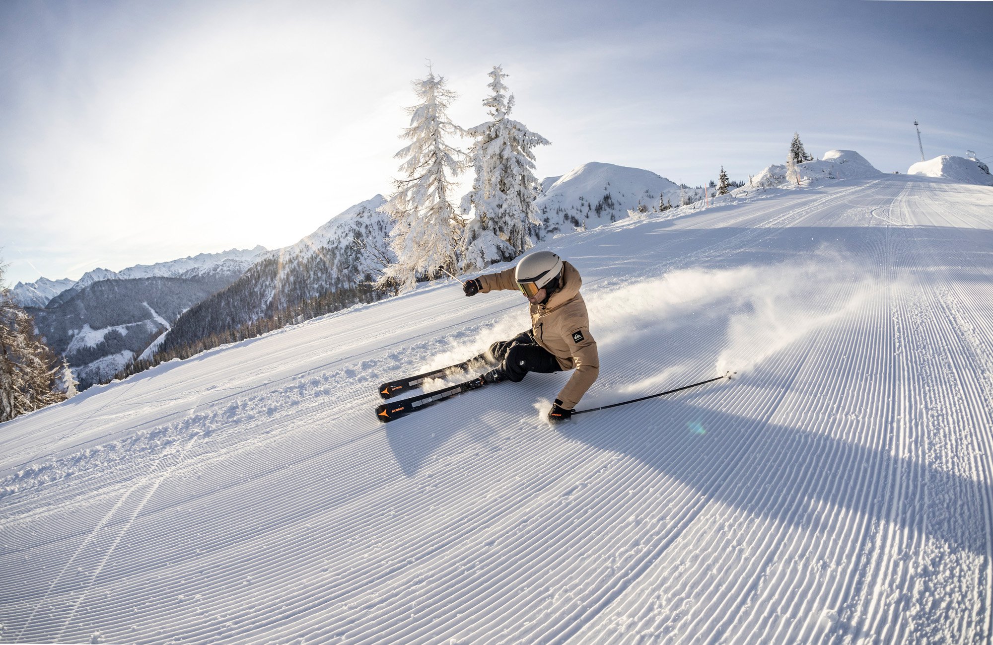 Ein Skifahrer fährt über eine perfekt präparierte Skipiste mit einer atemberaubenden Bergkulisse im Hintergrund.