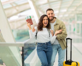 Copilot said:  Aufgeregter junger Mann und junge Frau, die am Flughafen fröhlich auf ihren Flug warten und gemeinsam Spaß haben | © Getty Images