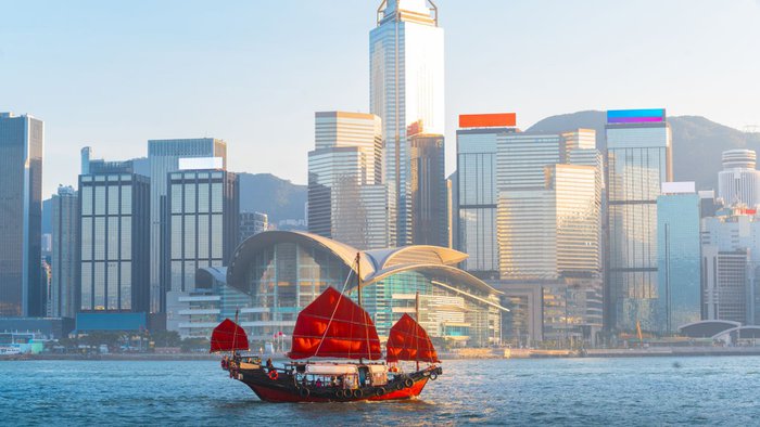 Traditionelle rote Dschunke mit Segeln auf dem Victoria Harbour vor der beeindruckenden Skyline von Hongkong bei Sonnenuntergang | © Getty Images