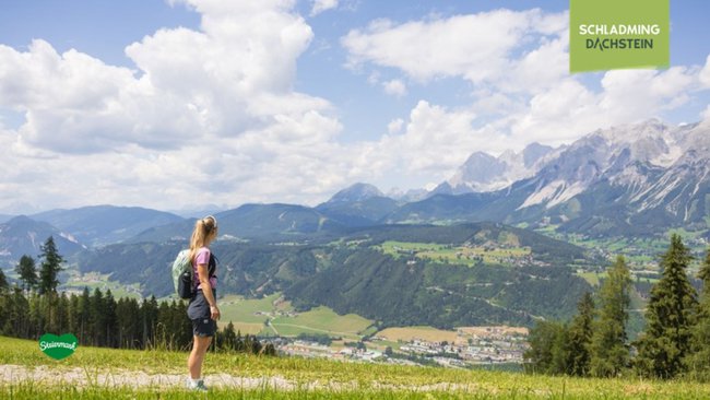 Eine Wanderin genießt die Ruhe und Schönheit der beeindruckenden Bergkulisse von Schladming-Dachstein.