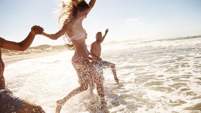 Zwei junge Paare, die am Strand durch das Wasser rennen | © Getty Images
