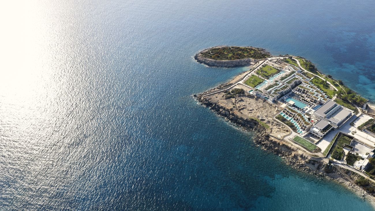 Vogelperspektive auf die weitläufige Anlage des Amoh a Luxury Collection Resort Rhodes, umgeben von türkisblauem Wasser, grüner Landschaft und elegant angelegten Gebäuden | © Amoh a Luxury Collection Resort Rhodes