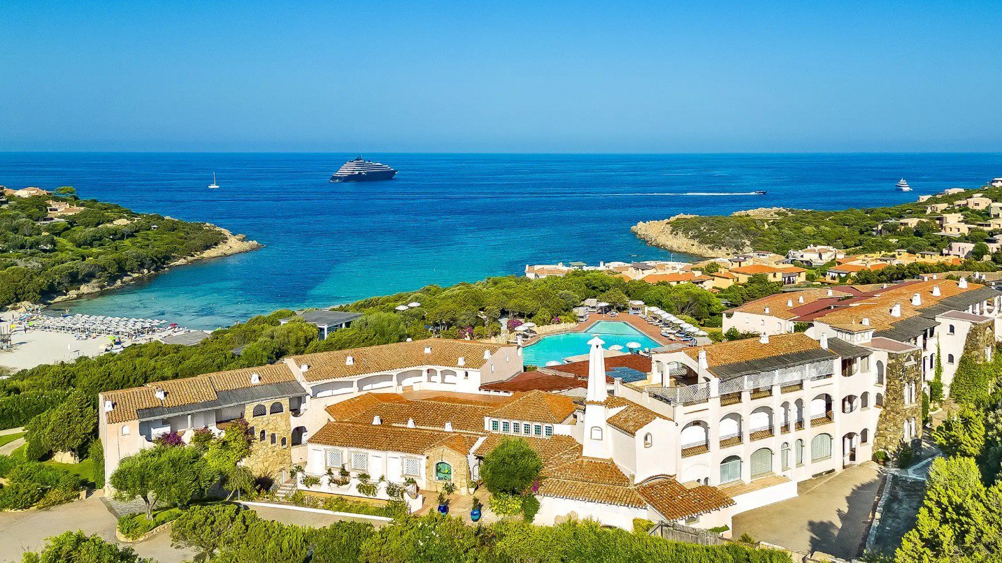 Luftaufnahme des Grand Hotels in Porto Cervo mit Blick auf die mediterrane Architektur der Anlage, den feinsandigen Strand und das blaue Meer im Hintergrund | © Grand Hotel in Porto Cervo
