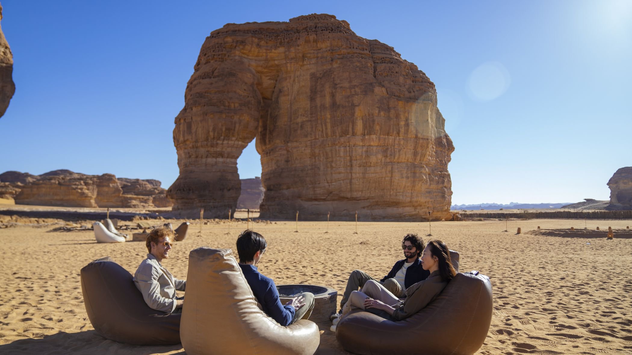 Gruppe von Menschen sitzt auf Sitzsäcken vor dem Elephant Rock in AlUla | © Saudi Tourism Authority