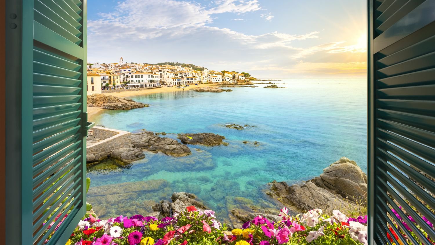 Blick durch ein offenes Fenster auf Strand, felsige Küste und die weiß getünchte Stadt Calella de Palafrugell an der Costa Brava bei Sonnenuntergang | © Getty Images