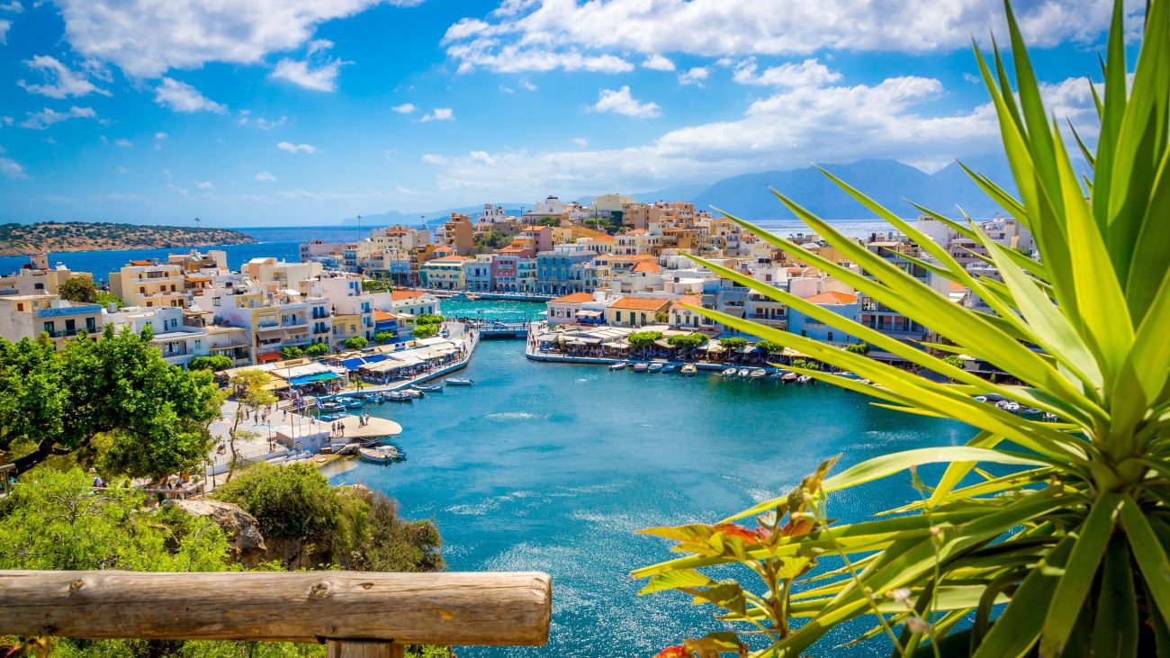 Traumblick auf Agios Nikolaos auf Kreta mit der Hafenstadt, sanften Hügeln und glitzerndem Mittelmeer | © Adobe Stock