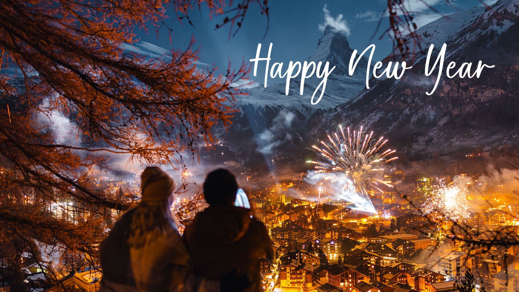 Zwei Personen betrachten ein Feuerwerk über einem beleuchteten Tal, umgeben von schneebedeckten Bergen | © Lufthansa City Center