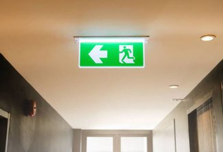 Das beleuchtete Fluchtwegschild weist mit einem Pfeil auf den Notausgang hin.