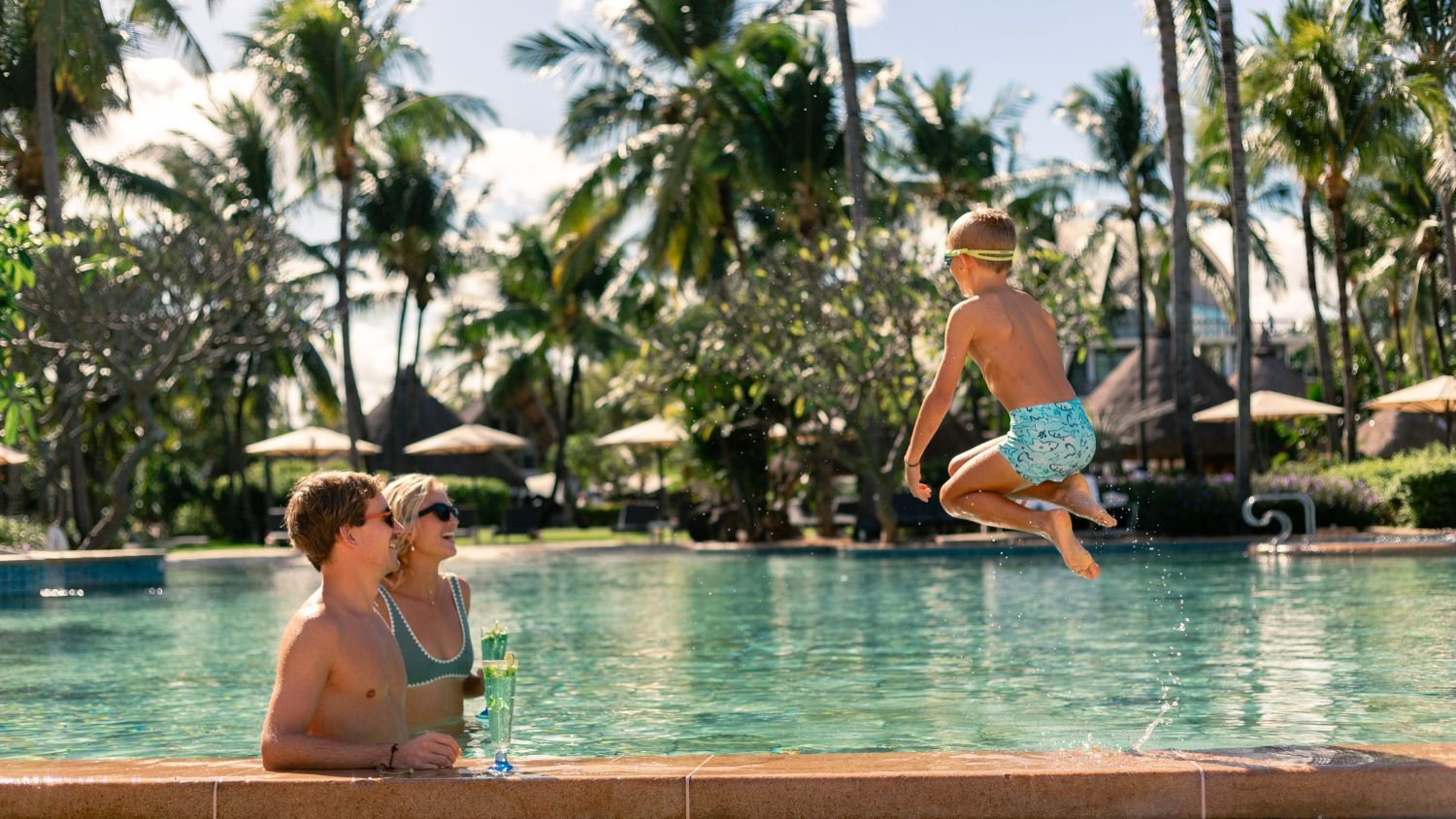 Eltern beobachten ihren Sohn, wie er fröhlich in den Pool des La Pirogue Mauritius springt, umgeben von entspannter tropischer Urlaubsatmosphäre | © Sunlife Mauritius