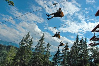Mehrere Personen gleiten an parallel gespannten Stahlseilen der Stoderzinken Zipline rasant talwärts.
