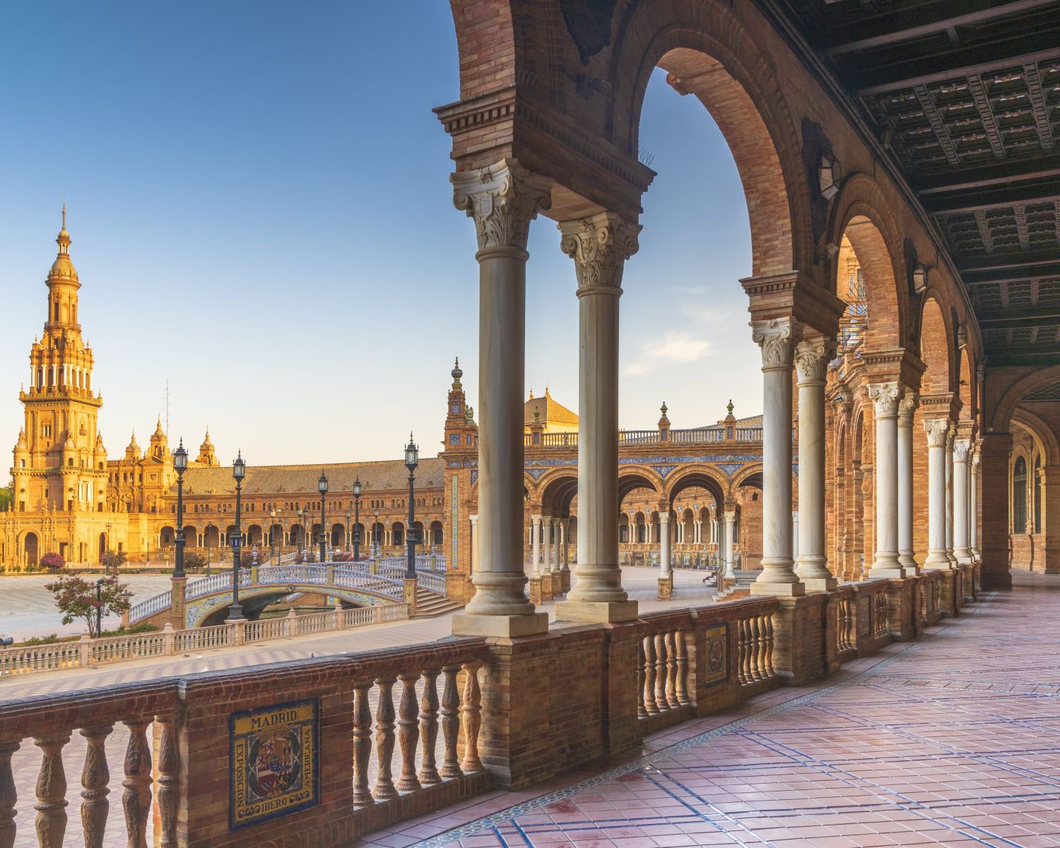 Blick von der Kolonnade des halbkreisförmigen Portikus auf die Plaza de España in Sevilla bei Sonnenaufgang, mit einem alten Turm im Hintergrund | © Getty Images
