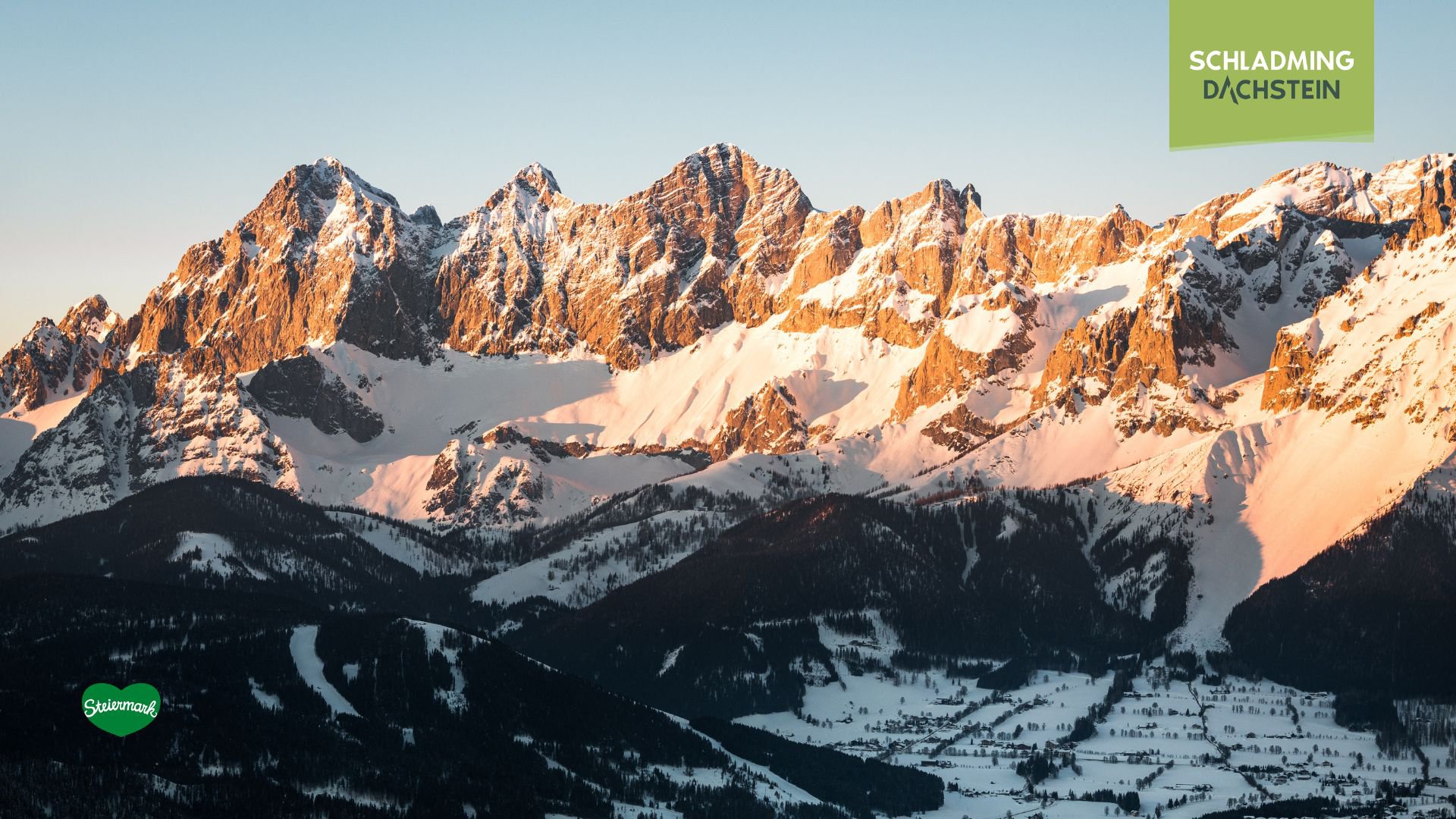 Der schneebedeckte Dachstein erhebt sich majestätisch unter dem klaren Abendhimmel. Die letzten Sonnenstrahlen des Tages tauchen die weißen Gipfel in ein warmes, goldenes Licht.