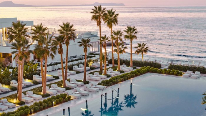 Pool des Grecotel LUX®ME White auf Kreta in der Dämmerung mit Blick auf das Meer und die beleuchtete Hotelanlage | © Grecotel Hotels & Resorts